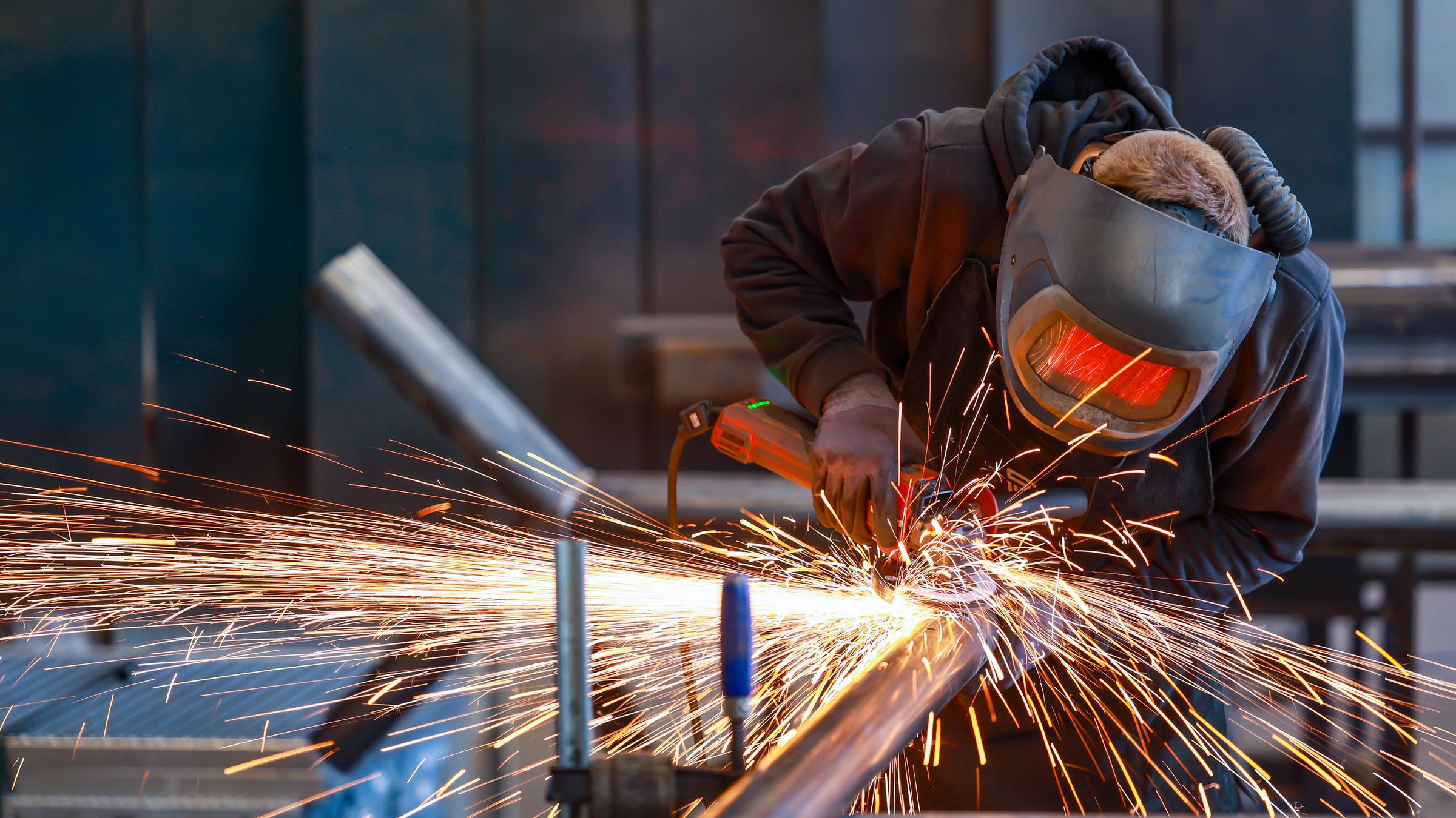 Ein Industriearbeiter flext mit einem Winkelschleifer ein Stahlrohr