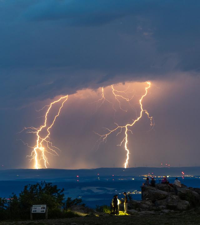 19.06.2026, Hessen, Schmitten: Menschen beobachten Blitze eines Gewitters am Großen Feldberg im Taunus.