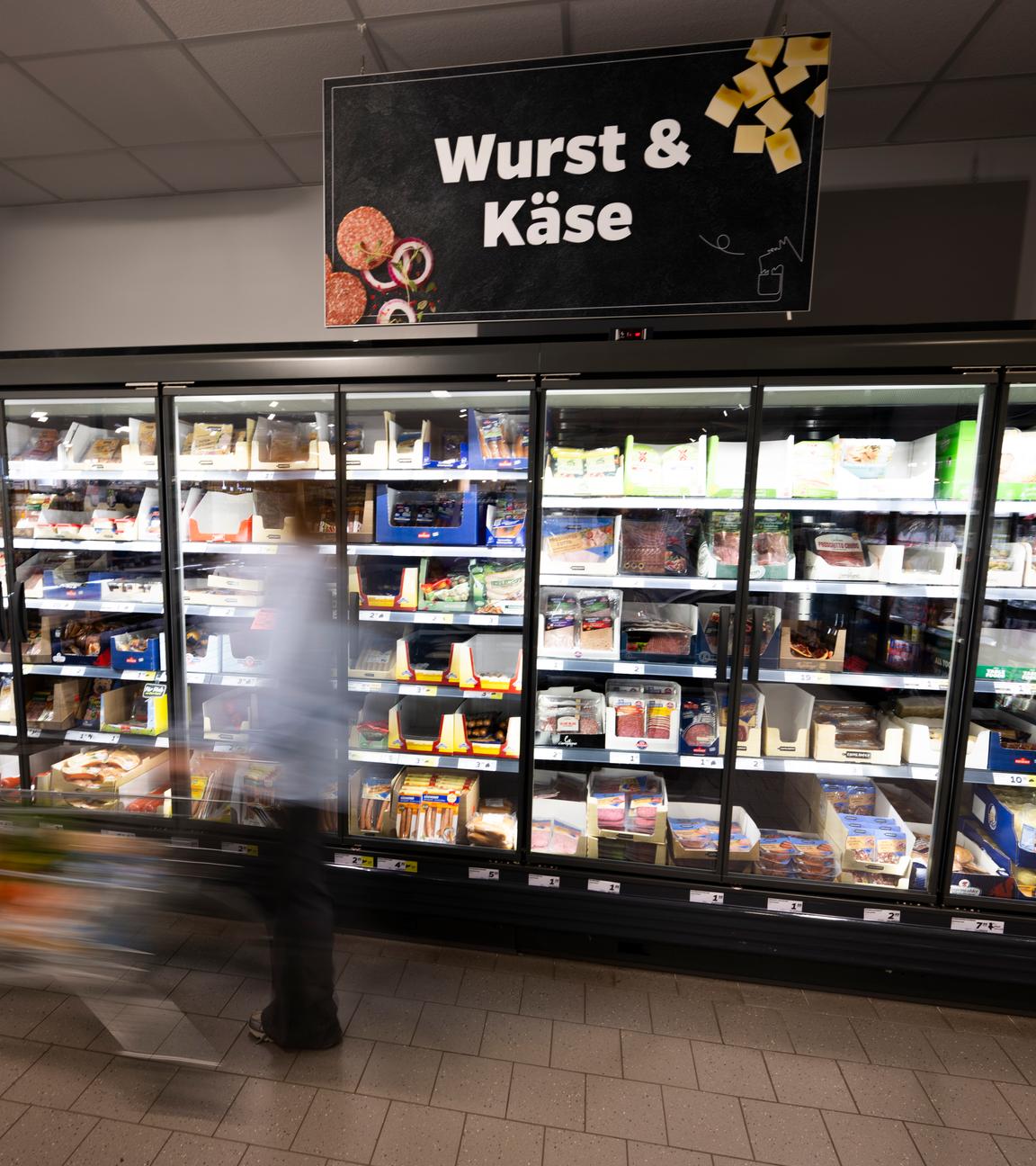 Eine Frau fährt mit ihrem Einkaufswagen vor dem Kühlregal eines Supermarkts. Mit dem "Deutschlandkorb" schlägt die SPD dem Lebensmittelhandel vor, Preise für bestimmte Grundnahrungsmittel freiwillig zu begrenzen. 