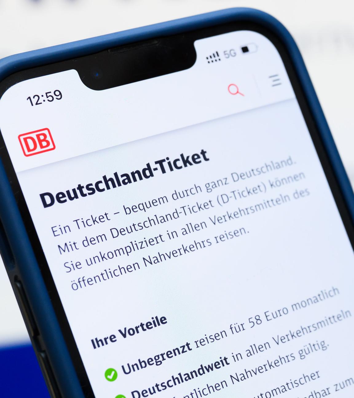 Eine Person hält am Hauptbahnhof ein Smartphone in der Hand, auf dessen Display eine Information zum Kauf des Deutschlandtickets zu sehen ist, während sie vor einem Fahrkartenautomaten steht.
