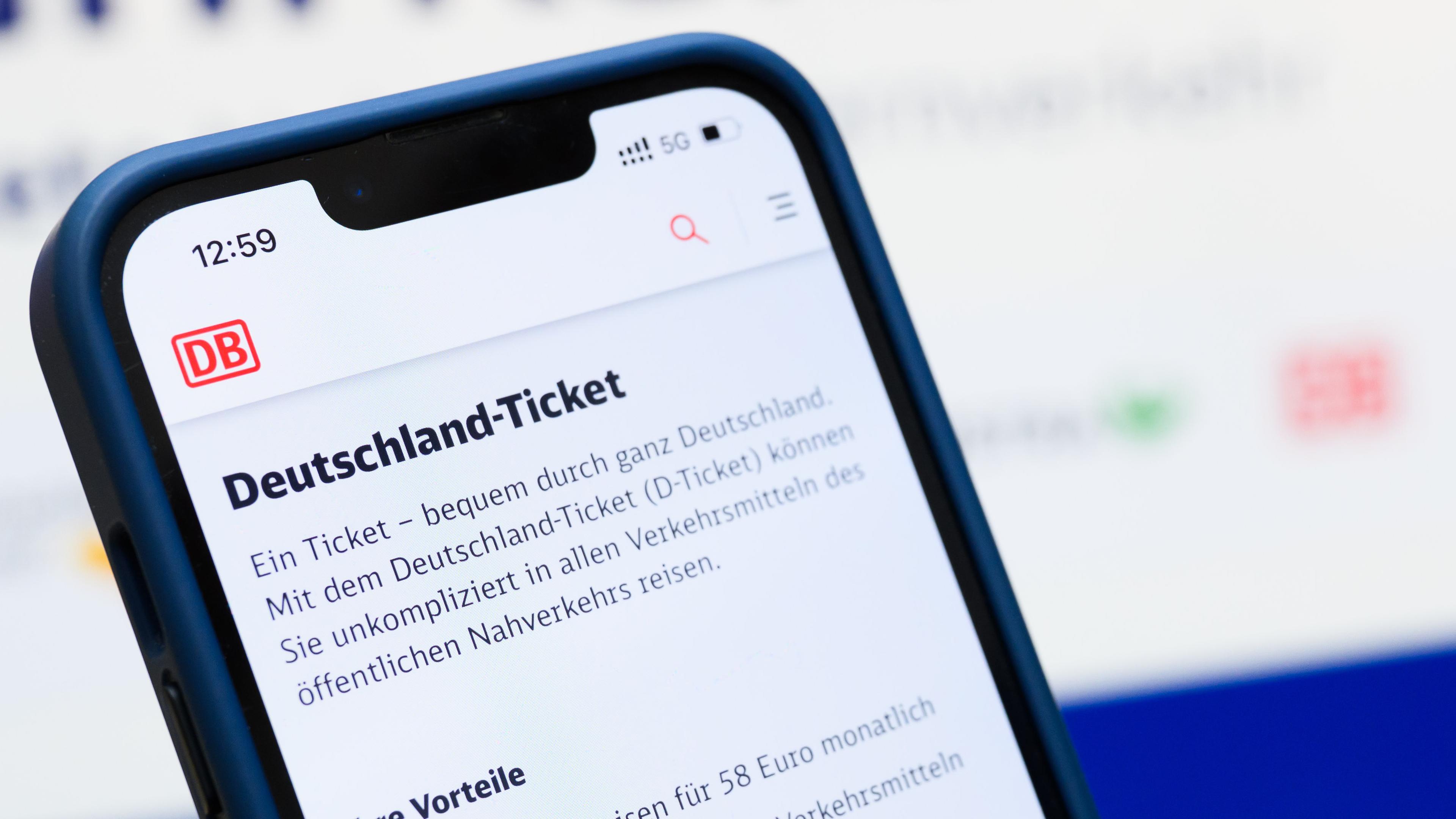 Eine Person hält am Hauptbahnhof ein Smartphone in der Hand, auf dessen Display eine Information zum Kauf des Deutschlandtickets zu sehen ist, während sie vor einem Fahrkartenautomaten steht.