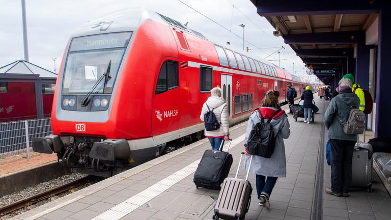Touristen laufen mit Rollkoffern am Bahnhof Norddeich-Mole entlang.