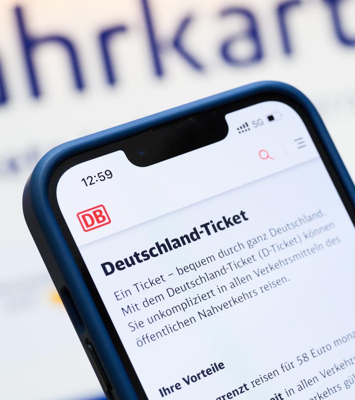Eine Person hält am Hauptbahnhof ein Smartphone in der Hand, auf dessen Display eine Information zum Kauf des Deutschlandtickets zu sehen ist, während sie vor einem Fahrkartenautomaten steht. 