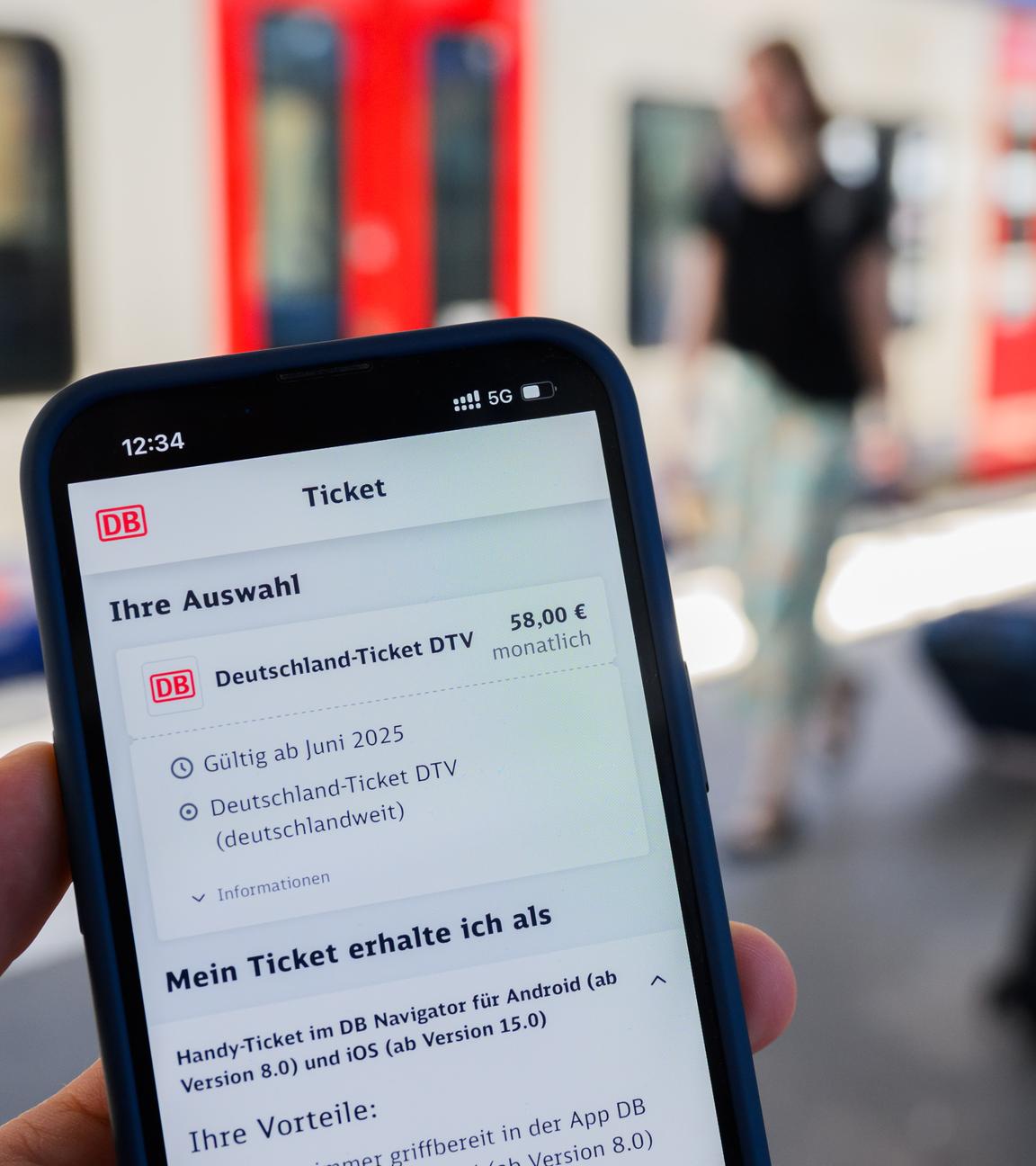 Ein Handy mit der Buchung eines Deutschlandtickets über die DB.Im Hintergrund ist verschwommen ein Zug