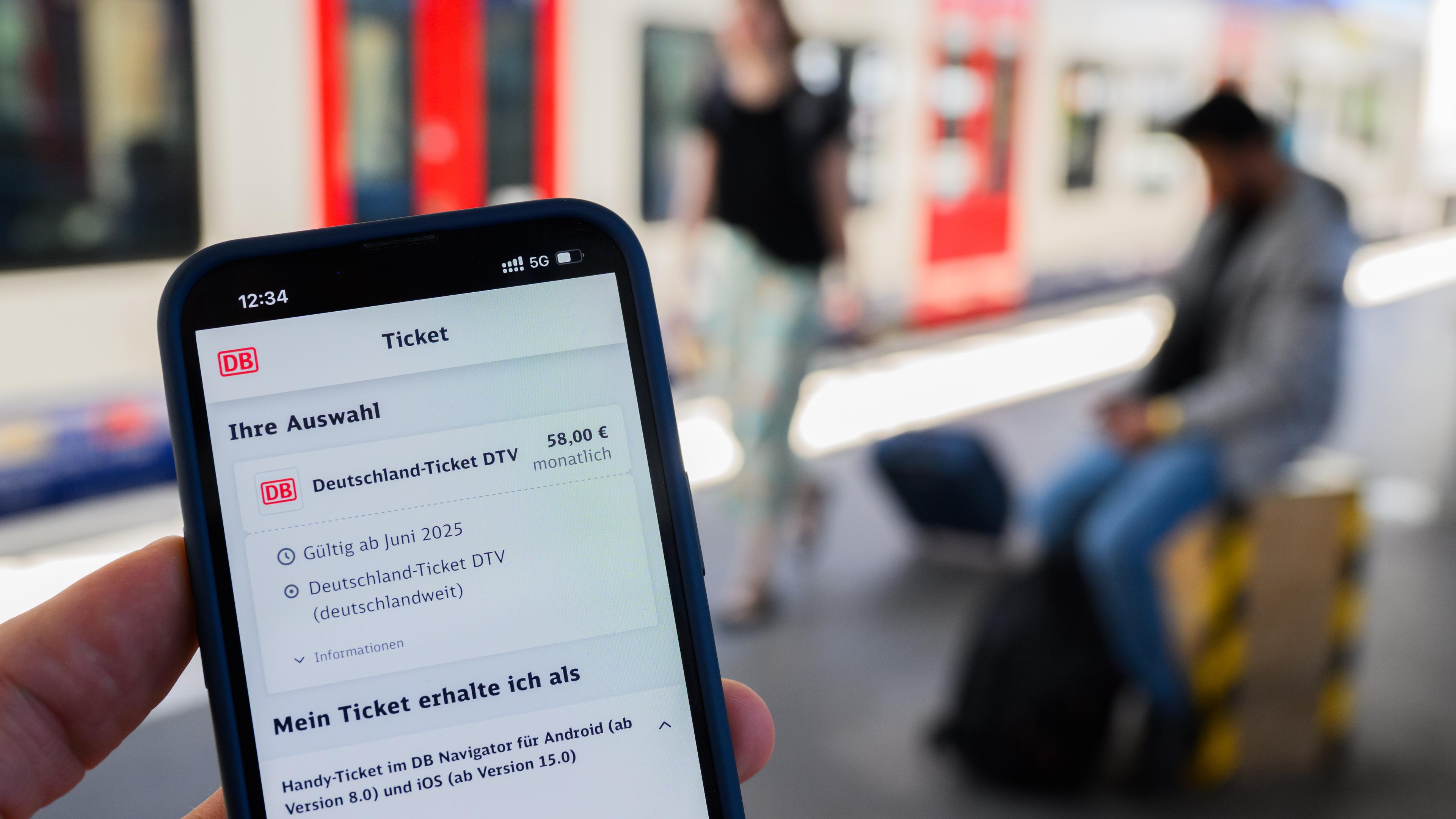 Ein Handy mit der Buchung eines Deutschlandtickets über die DB.Im Hintergrund ist verschwommen ein Zug