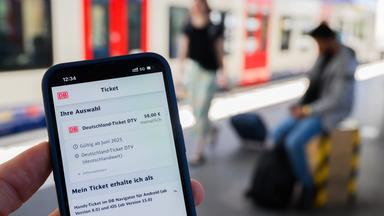 Ein Handy mit der Buchung eines Deutschlandtickets über die DB.Im Hintergrund ist verschwommen ein Zug