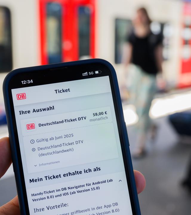 Ein Handy mit der Buchung eines Deutschlandtickets über die DB.Im Hintergrund ist verschwommen ein Zug