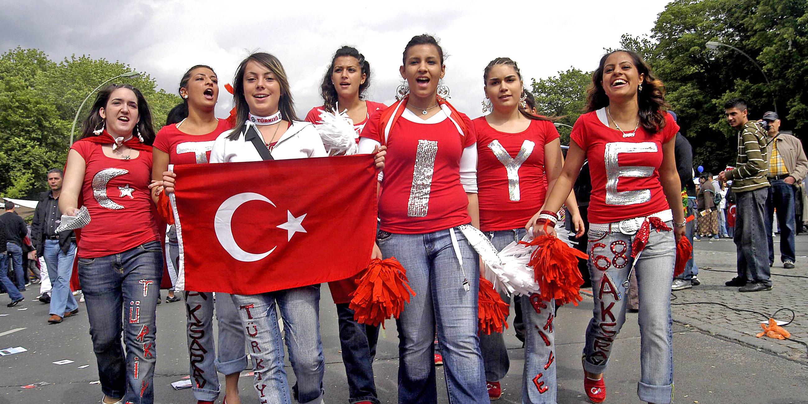 Eine Gruppe junger Frauen, auf deren roten T-Shirts Buchstaben stehen, die das Wort Türkiye ergeben, laufen mit einer türkischen Flagge auf einer Straße.
