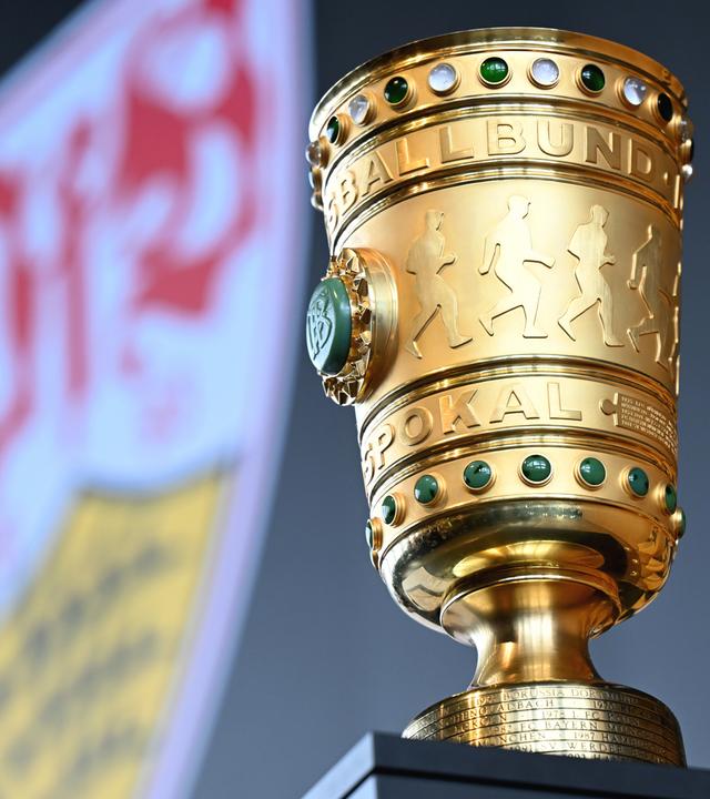 Der DFB-Pokal steht auf einem Tisch, im Hintergrund das Logo von Pokalverteidiger VfB Stuttgart.