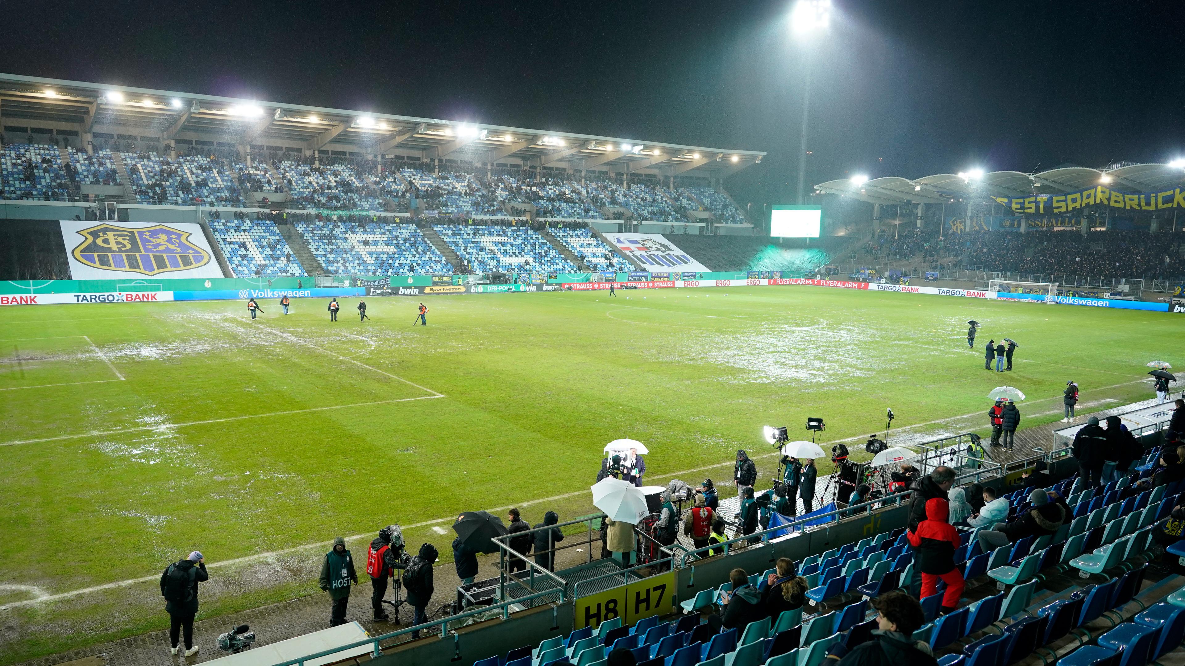 07.02.2024, Saarbrücken: DFB-Pokal, 1. FC Saarbrücken - Bor. Mönchengladbach, Viertelfinale im Ludwigspark-Stadion. Arbeiter versuchen, Wasserlachen vom Spielfeld zu entfernen. 