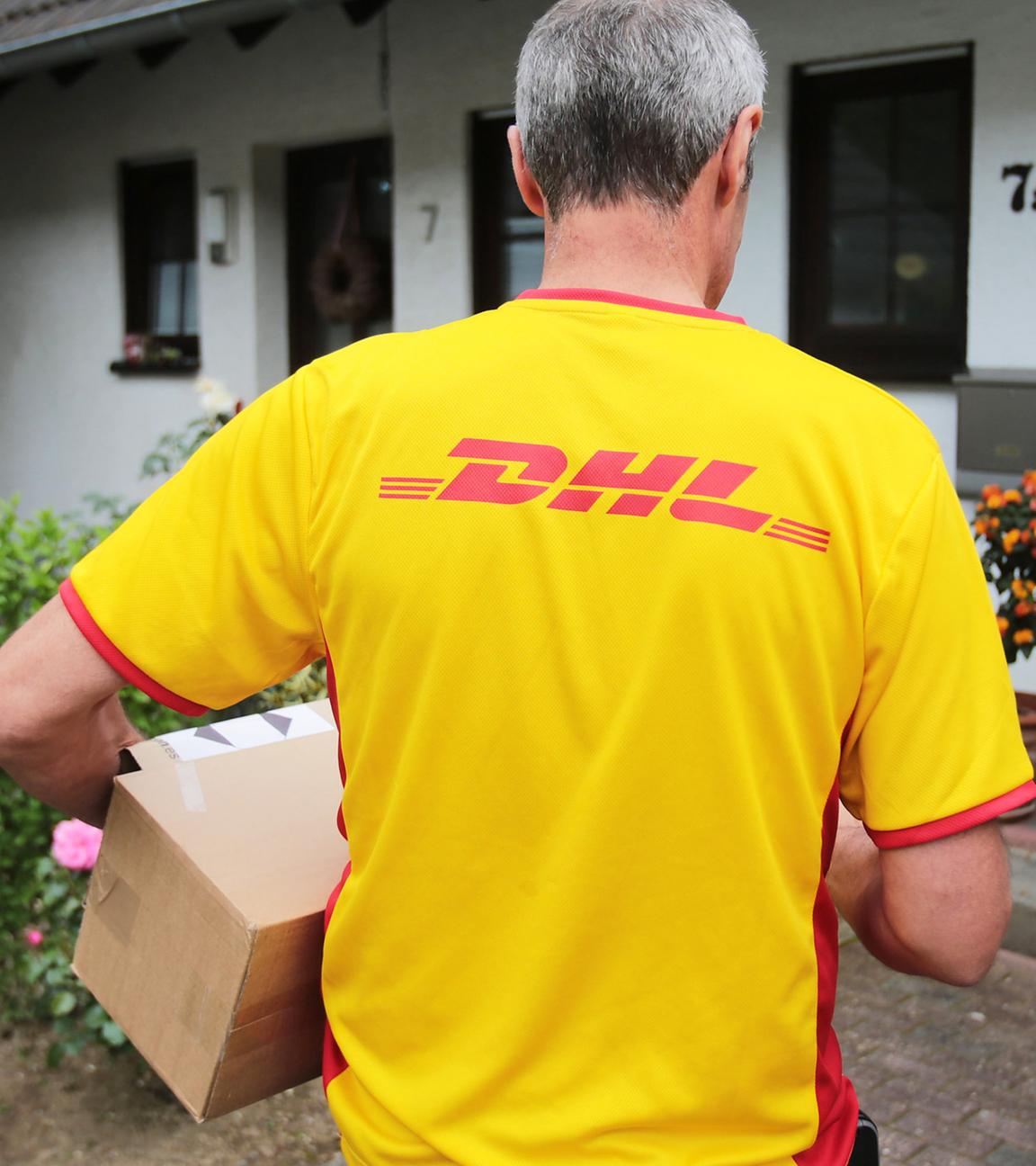 Paketbote von DHL trägt Paket aus