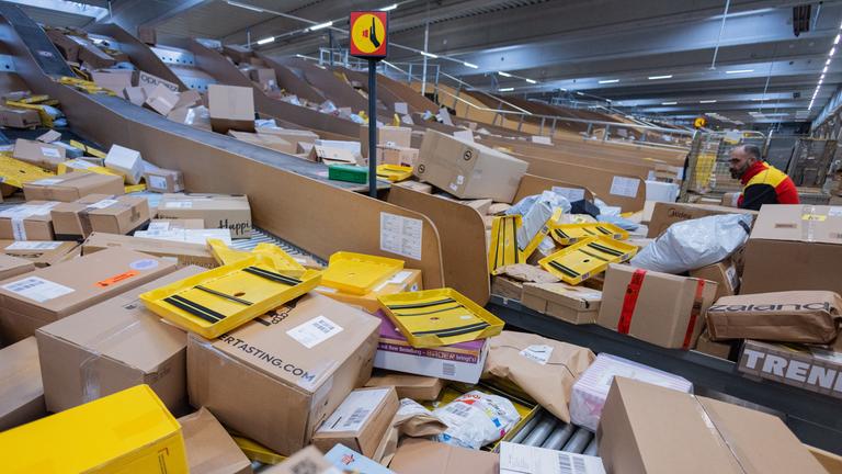 Ein Paketzusteller sortiert und räumt in einer Zustellbasis von Deutsche Post DHL Pakete in ein Zustellfahrzeug.