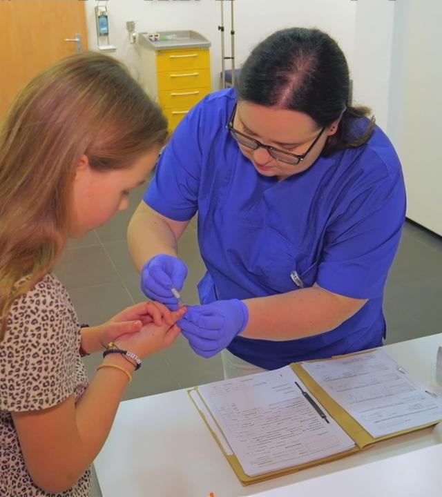 Eine Frau piekst einem Mädchen in einer Arztpraxis in den Finger, um ihren Blutzucker zu bestimmen