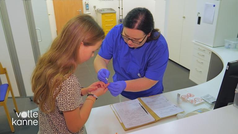 Eine Frau piekst einem Mädchen in einer Arztpraxis in den Finger, um ihren Blutzucker zu bestimmen
