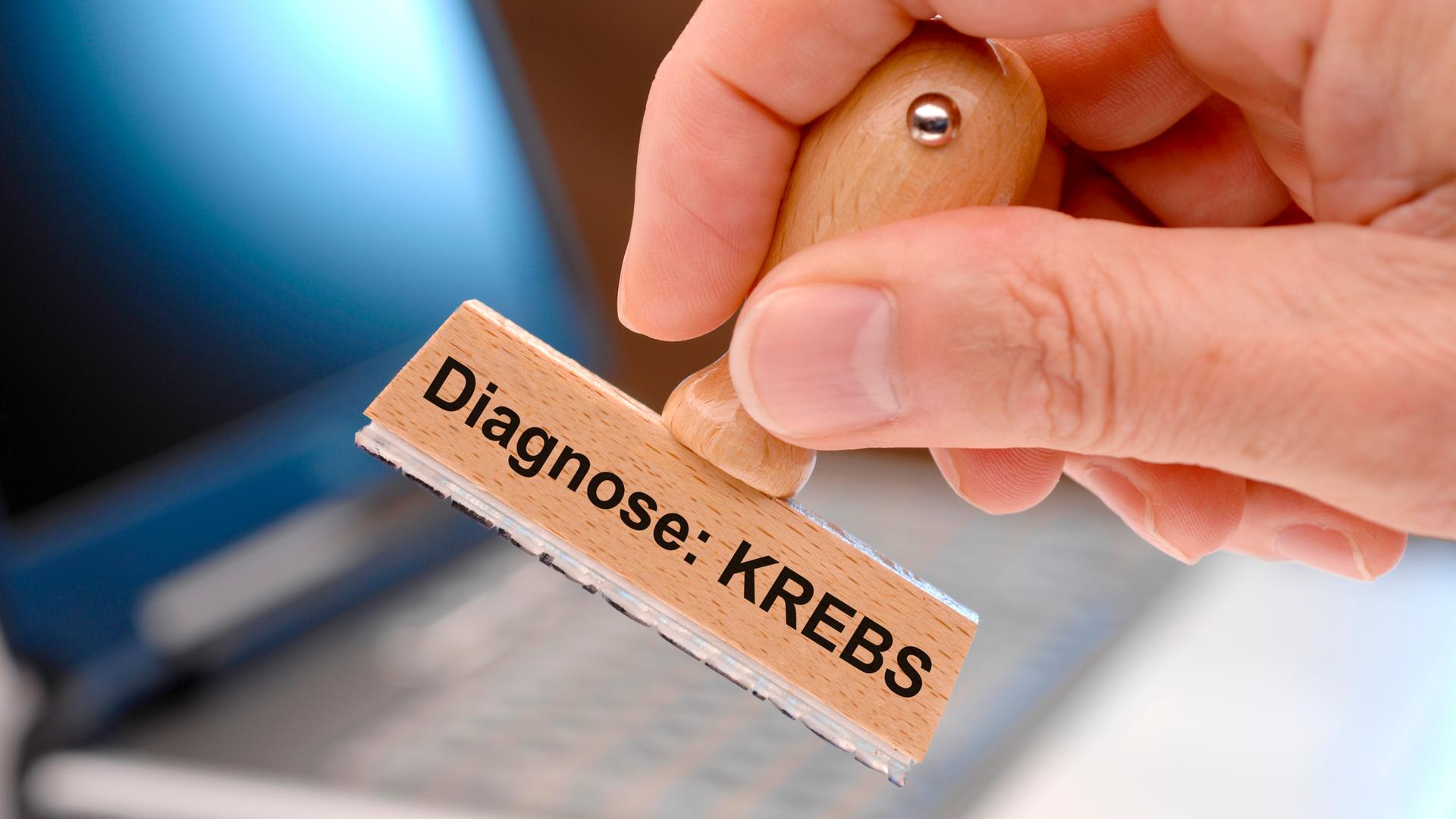 Eine Hand hält den Holzstempel mit der Aufschrift "Diagnose Krebs" in die Luft.