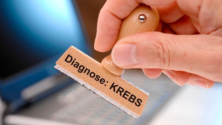 Eine Hand hält den Holzstempel mit der Aufschrift "Diagnose Krebs" in die Luft.