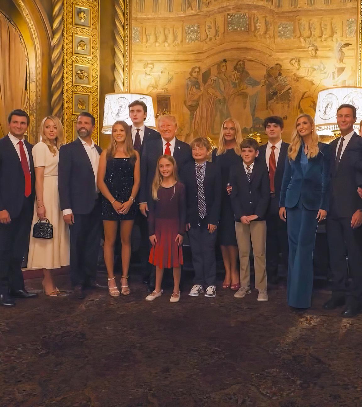 Donald Trump steht umringt von Familienmitgliedern und Elon Musk in einem prächtigen Foyer. Alle sind festlich gekleidet und posieren für ein Foto.