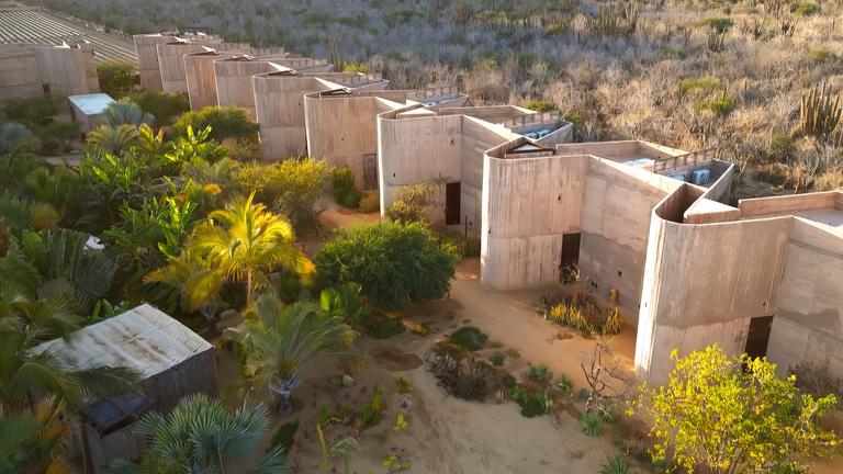 Luftbild: Einer Reihe von modernen, rechteckigen Gebäuden steht in einer trockenen, bewachsenen Landschaft mit Büschen und Bäumen.