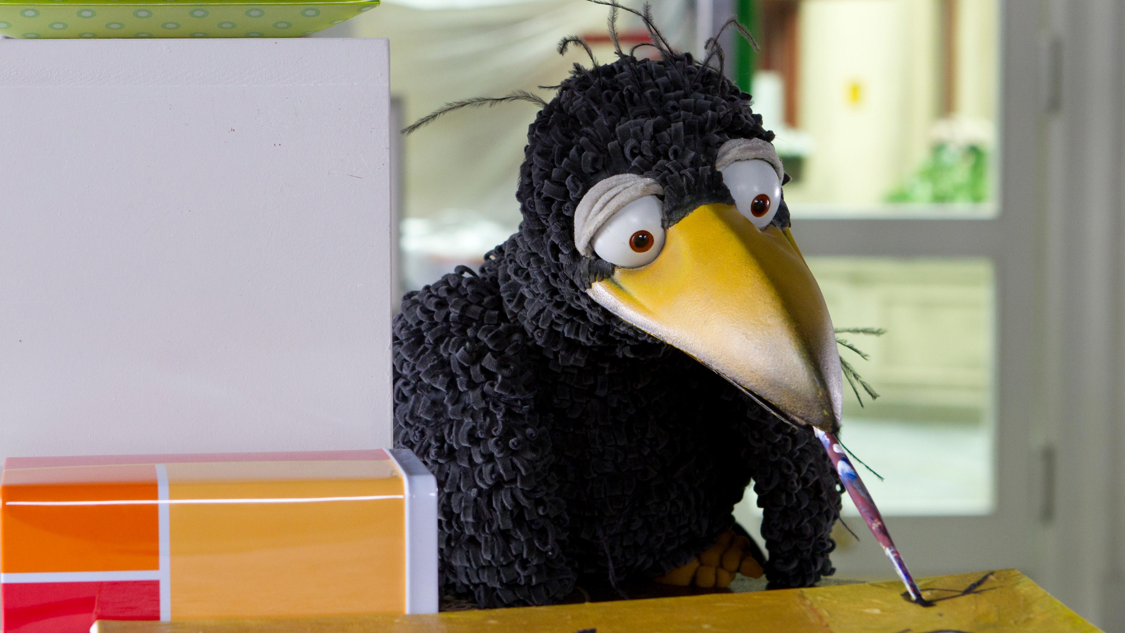 Rabe Rudi hat einen Pinsel im Schnabel und malt ein Bild