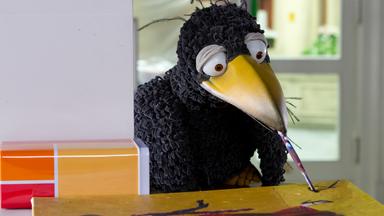 Rabe Rudi hat einen Pinsel im Schnabel und malt ein Bild