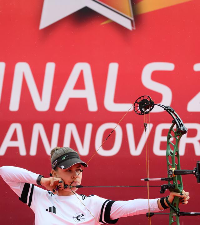 Eine Bogenschützin spannt ihren Bogen vor dem Logo der "Finals"