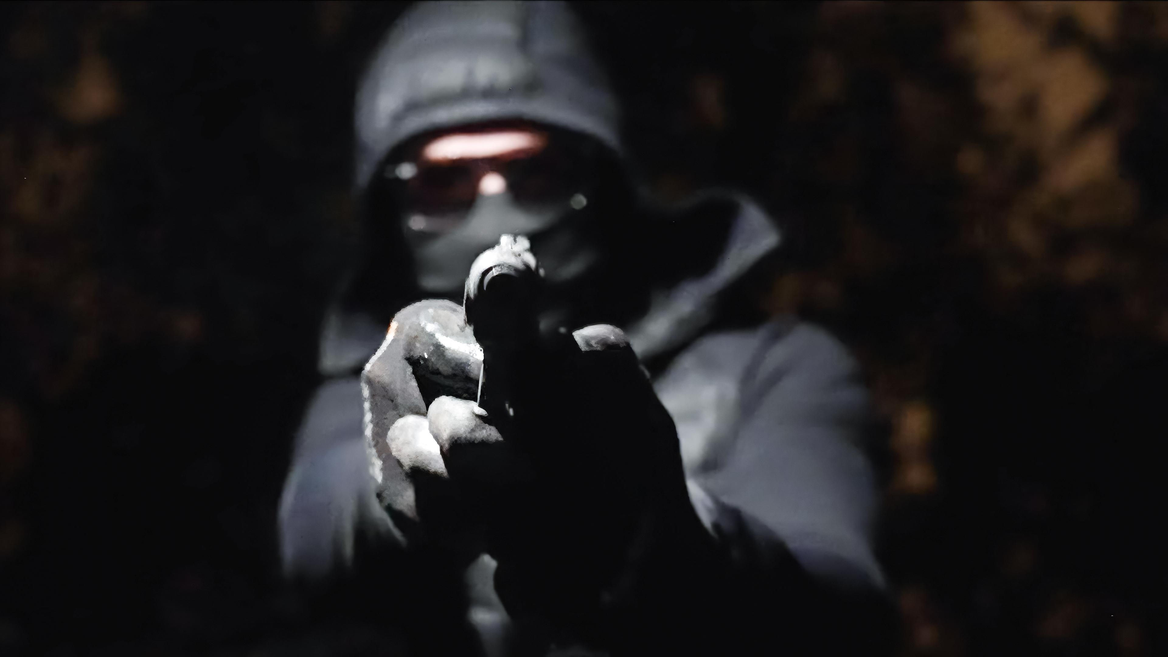 In der Dunkelheit hält ein vermummter Mann eine Waffe in den Händen und zielt damit geradeaus.