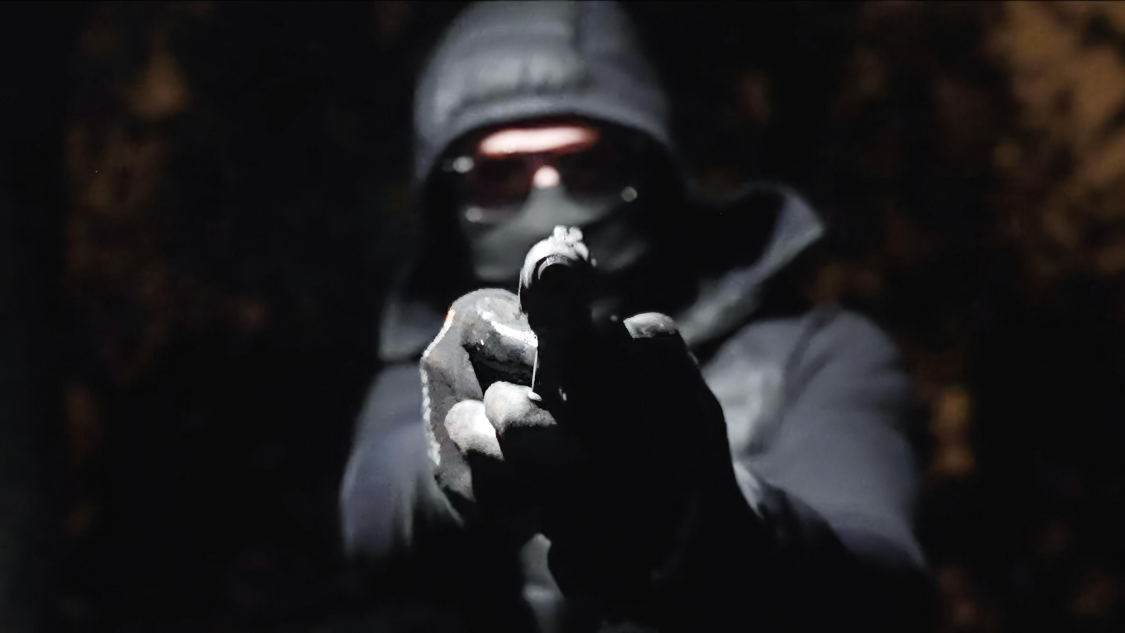 In der Dunkelheit hält ein vermummter Mann eine Waffe in den Händen und zielt damit geradeaus.