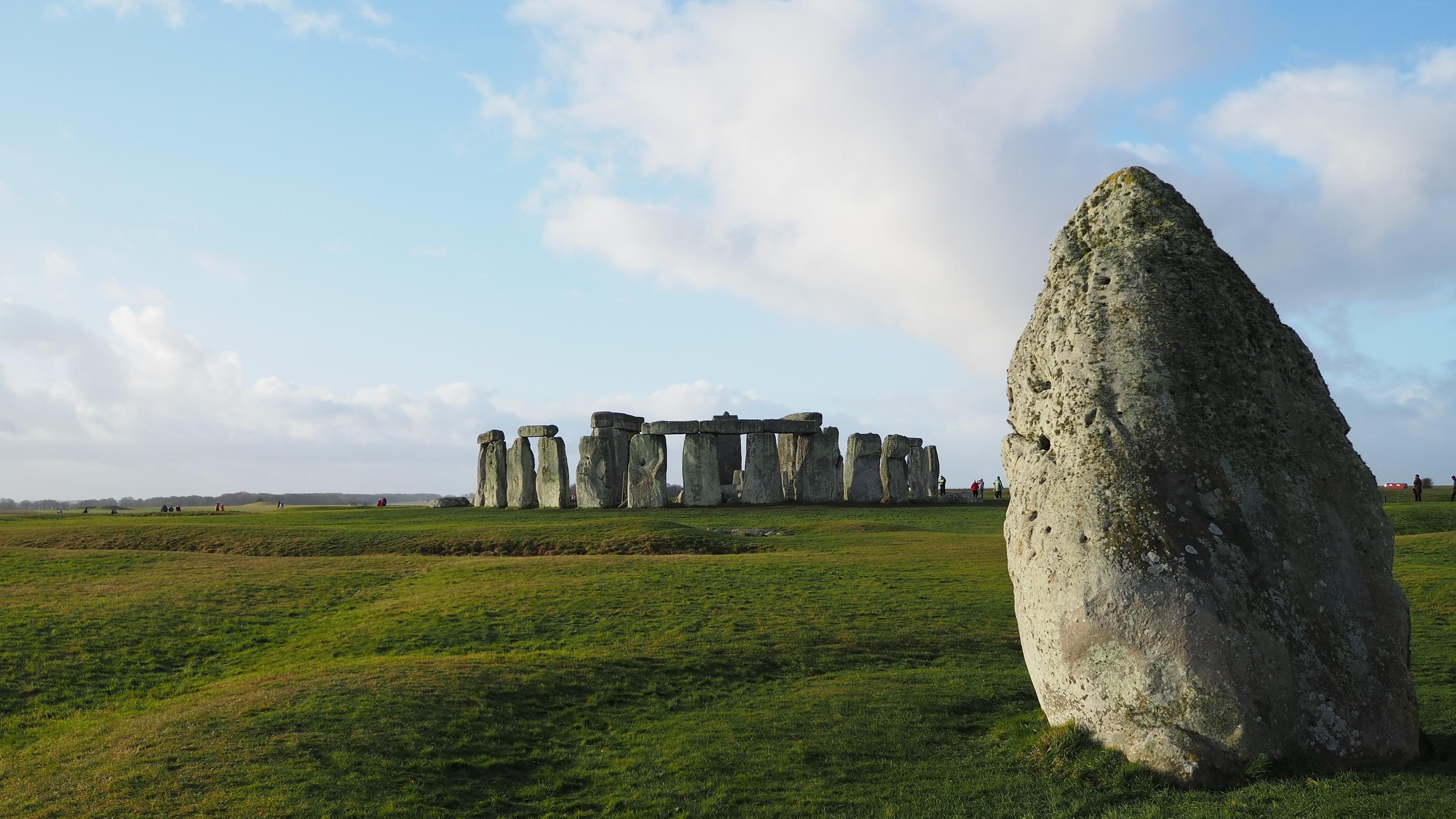 Im Hintergrund ein Steinkreis aus riesigen Megalithen. Im Vordergrund ein weiterer Megalith auf einer Rasenfläche.