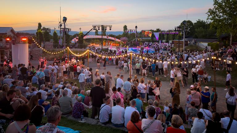 In der Abenddämmerung sitzen und stehen die Besuchenden auf dem Gelände bei "Die große Sommerparty".