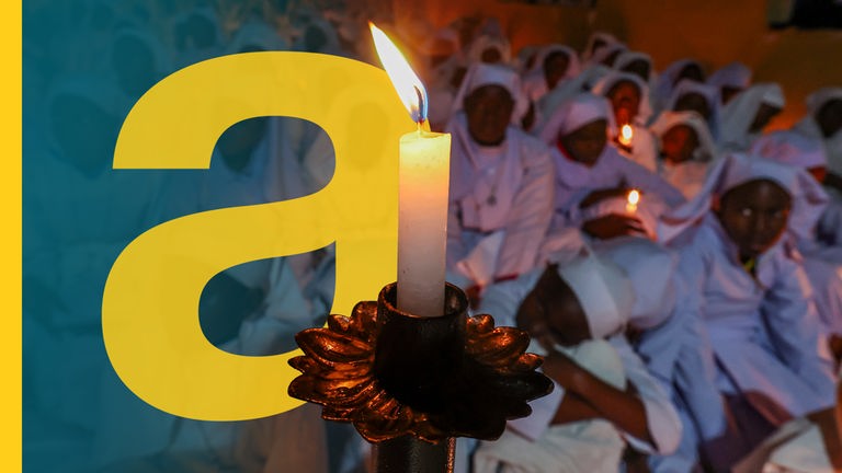 Eine Kerze im Vordergrund, im Hintergrund betetende Katholiken