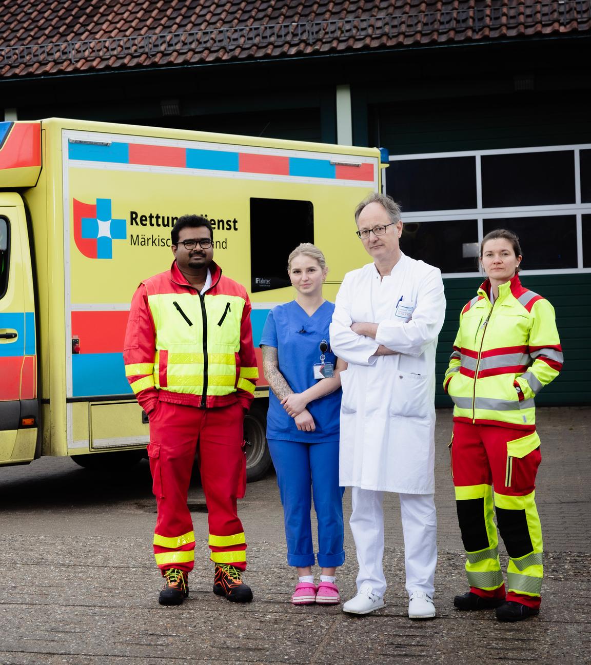 Vier Personen stehen vor einem gelben Rettungswagen mit rot-blauen Quadraten und der Aufschrift "Rettungsdienst Märkisch-Oderland": Anoop Puritipati (35, Assistenzarzt), Janina Buhe (24, Krankenpflegerin), Georg Bauer (58, Chefarzt) und Julia Kraushaar (35, Assistenzärztin).