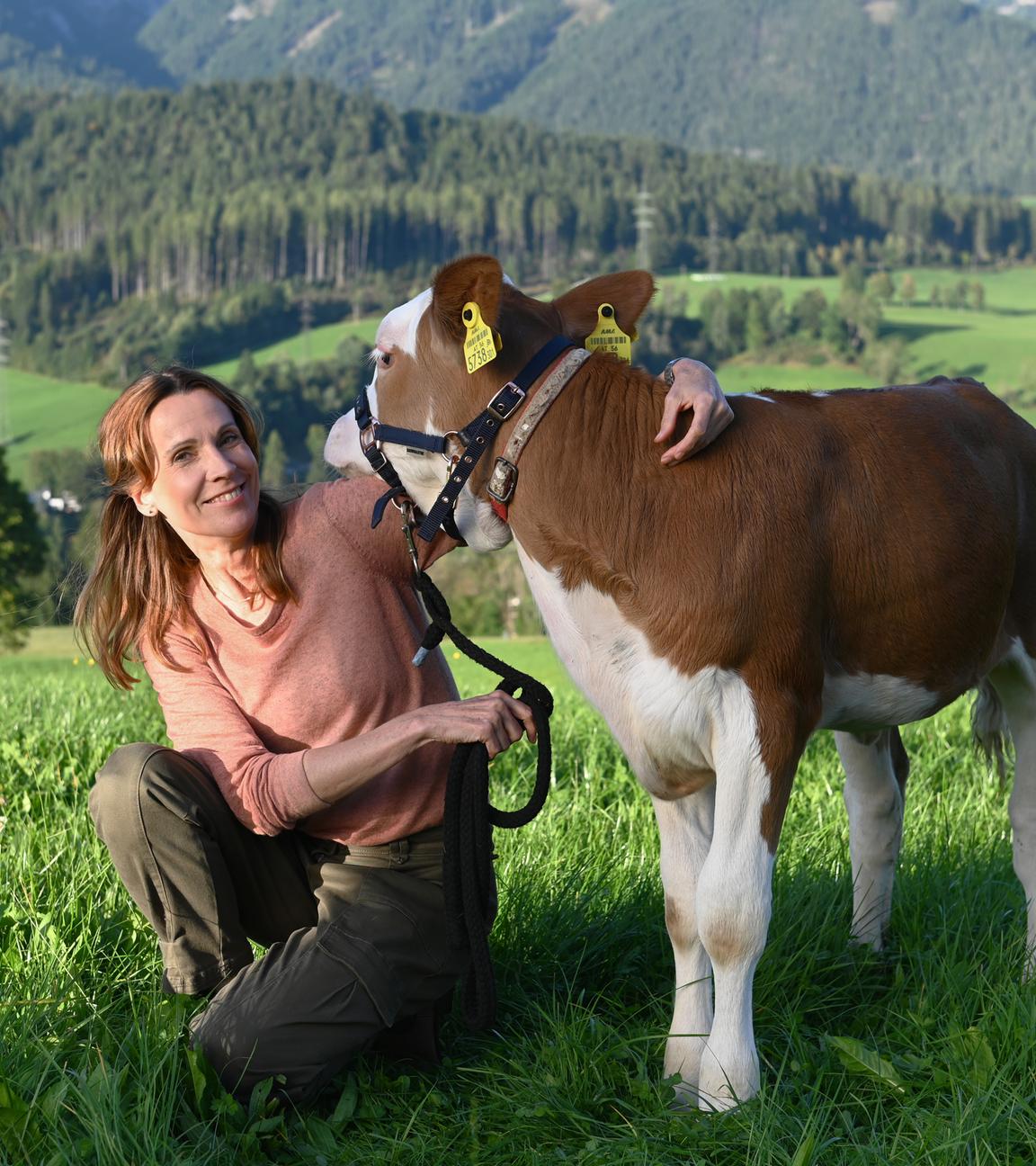 Die Schauspielerin Doris Schretzmayer in einer Wiese mit einem Kalb.