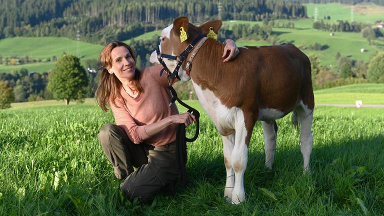 Die Schauspielerin Doris Schretzmayer in einer Wiese mit einem Kalb.