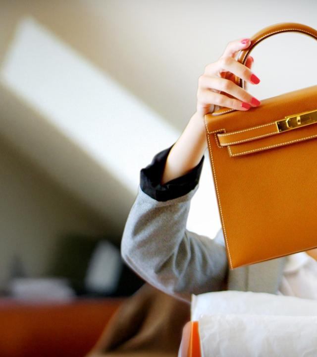 Frau packt stolz ihre neue Hermès Kelly aus und hält die Tasche vor ihrem Kopf in die Höhe.