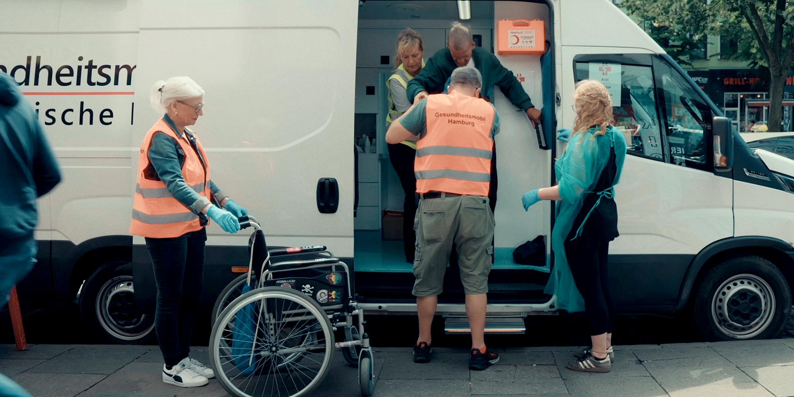 Menschen ohne Krankenversicherung fallen im Gesundheitssystem häufig durchs Raster – wie hier in Hamburg finden sie medizinische Hilfe in Gesundheitsmobilen. "Die Spur: Todkrank auf der Straße": Mehrere Personen stehen um das Gesundheitsmobil herum. 