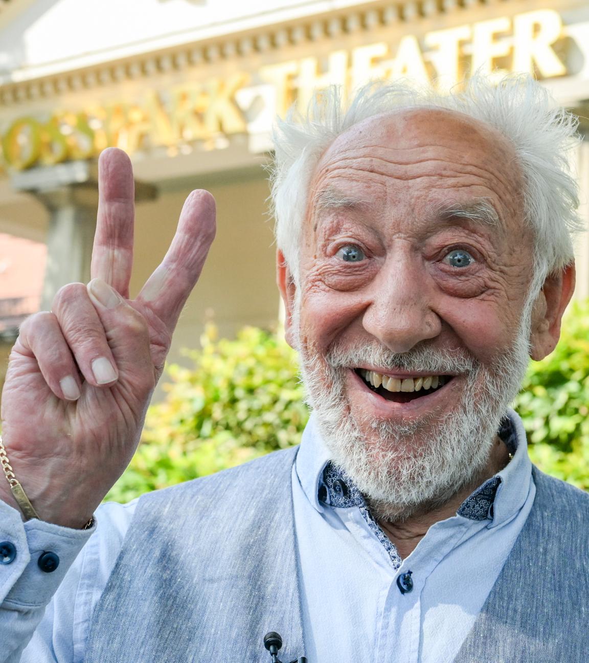 Dieter Hallervorden lächelt und macht ein Peace-Zeichen in die Kamera.