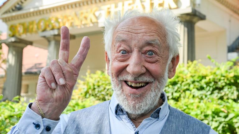 Dieter Hallervorden lächelt und macht ein Peace-Zeichen in die Kamera.