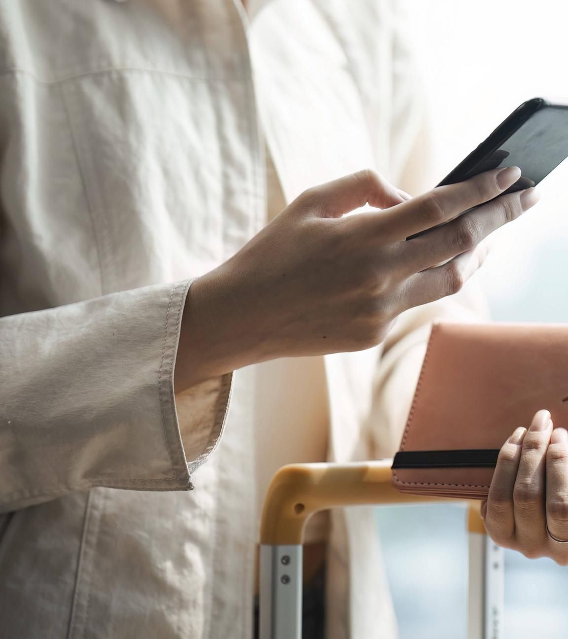 Symbolbild: Frau mit mobilen Smartphone und hält Reisepass mit Koffer