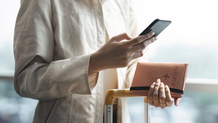 Symbolbild: Frau mit mobilen Smartphone und hält Reisepass mit Koffer