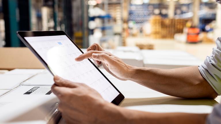 Hände eines Arbeiters, der einen Tablet-PC zur Überprüfung des Inventars im Lager benutzt