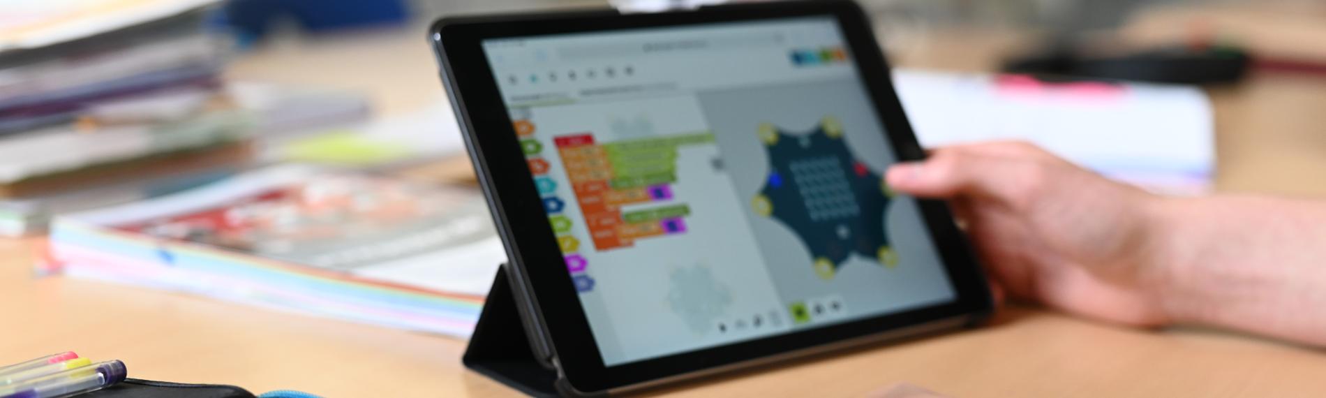 Auf einem Tisch in einer Schule steht ein Tablet, daneben liegt ein Federmäppchen mit Buntstiften.