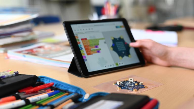 Auf einem Tisch in einer Schule steht ein Tablet, daneben liegt ein Federmäppchen mit Buntstiften.