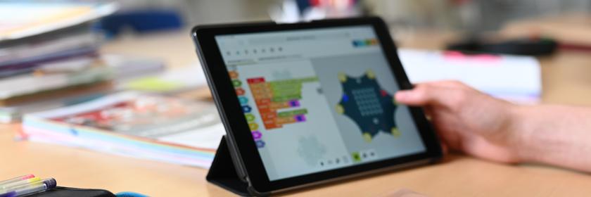 Auf einem Tisch in einer Schule steht ein Tablet, daneben liegt ein Federmäppchen mit Buntstiften.