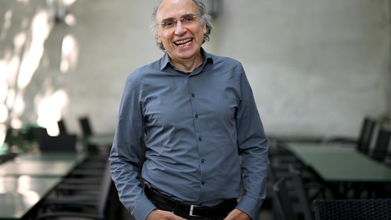 Porträtfoto eines Mannes mit kurzen lockigen graumelierten Haaren, Halbglatze und Brille.