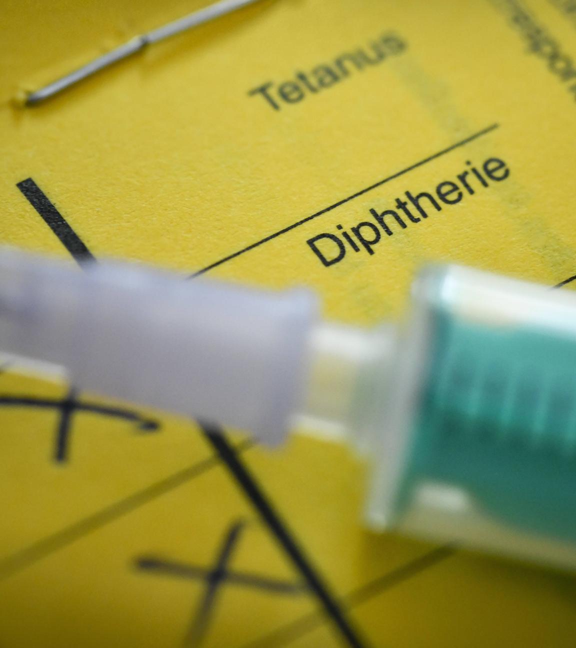 Nahaufnahme einer Spritze, die auf einem gelben Impfpass liegt.