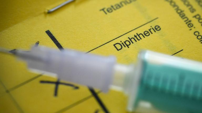 Nahaufnahme einer Spritze, die auf einem gelben Impfpass liegt.