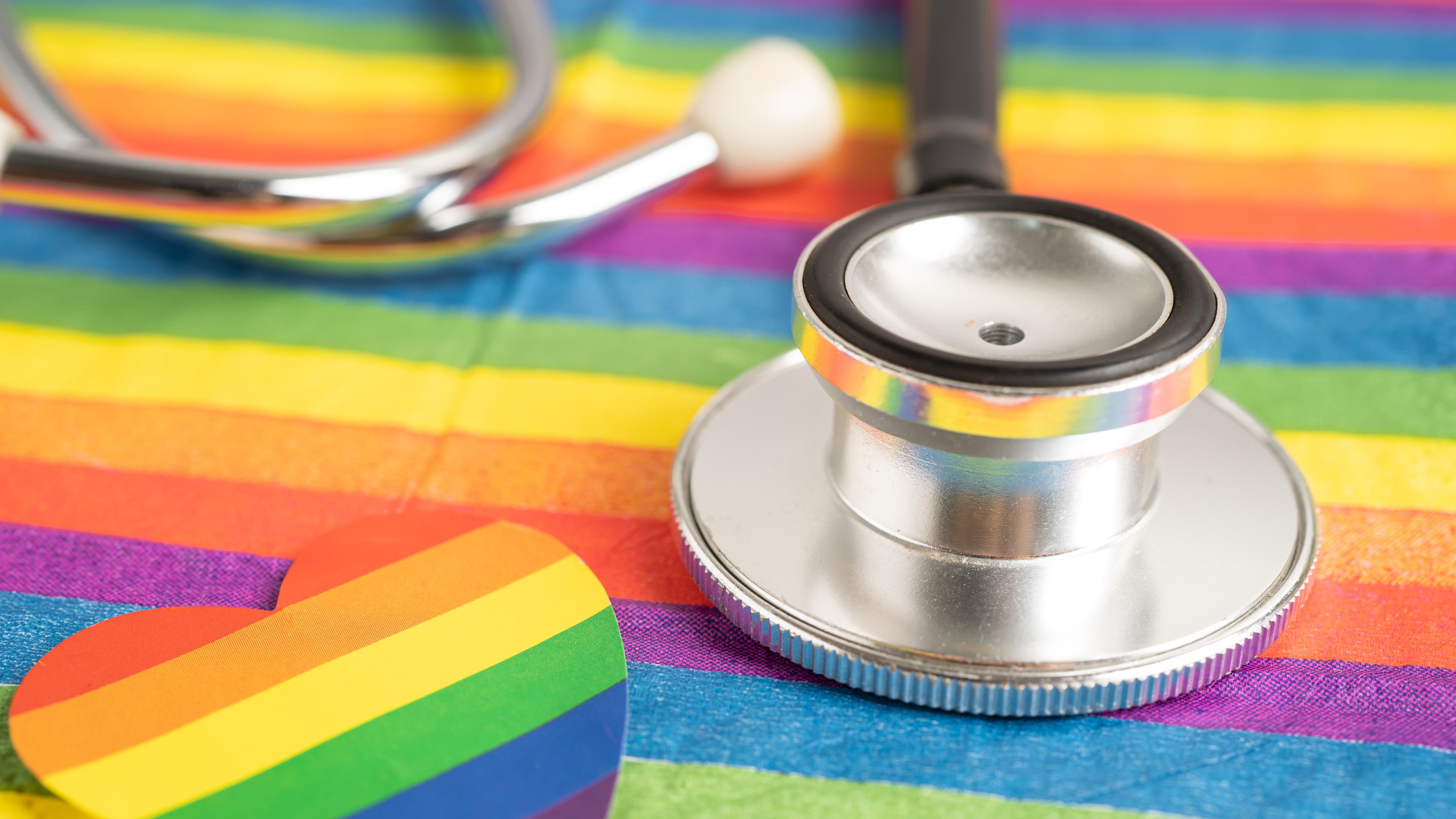 Zu sehen ist ein Stethoskop auf einer Regenbogenflagge.