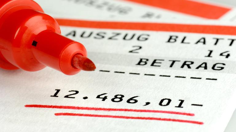 Auf einem Kontoauszug mit rot unterstrichenem Soll-Saldo liegt ein roter Filzstift.