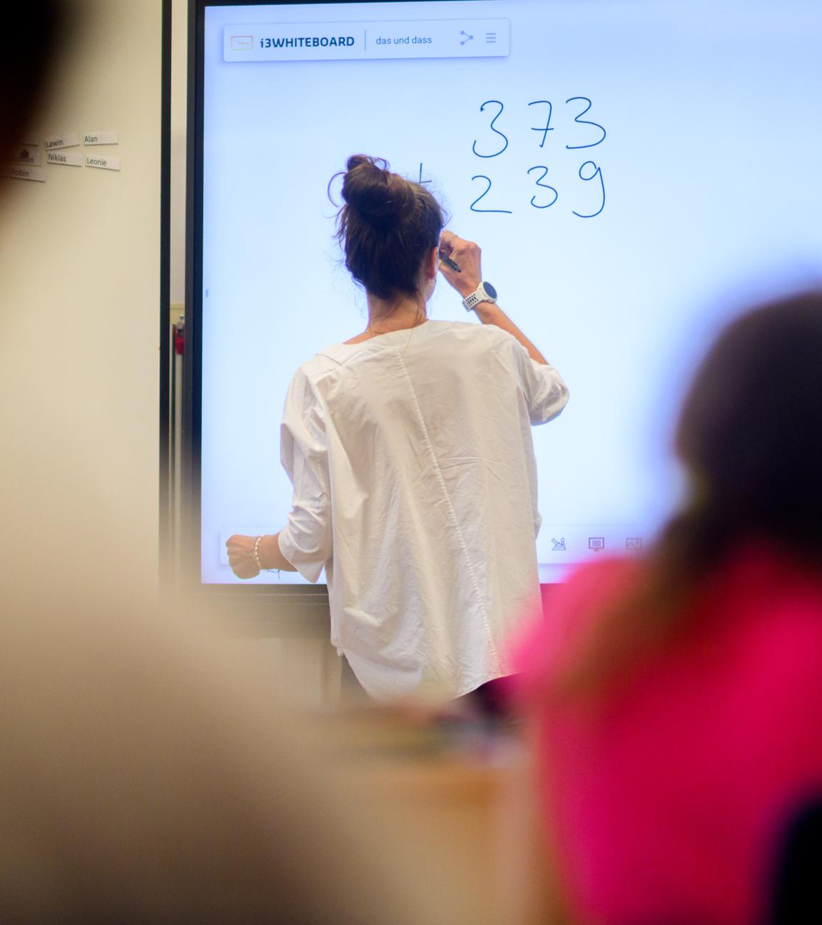 Eine Lehrerin schreibt eine Mathematikaufgabe auf eine digitale Schultafel.