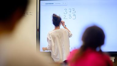 Eine Lehrerin schreibt eine Mathematikaufgabe auf eine digitale Schultafel.